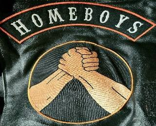 IT CONSISTS OF TWO SEPARATE PATCHES ONE AN UPPER ROCKER PATCH BLACK BACKGROUND ORANGE BORDER WITH THE WORD HOMEBOYS IN ALL CAPITAL WHITE LETTERS USING CARNIVAL FONT IN 2 IN SECOND IS A 9 IN ROUND PATC